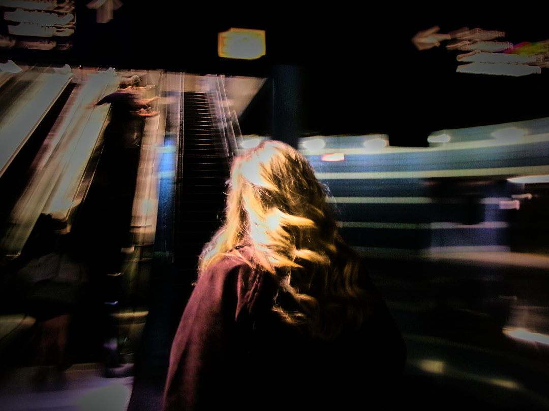 A woman with long hair at the foot of an escalator, in motion blur