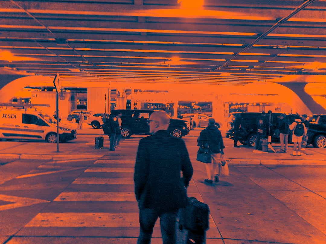 A man with a suitcase crossing to the pickup lanes under the terminal