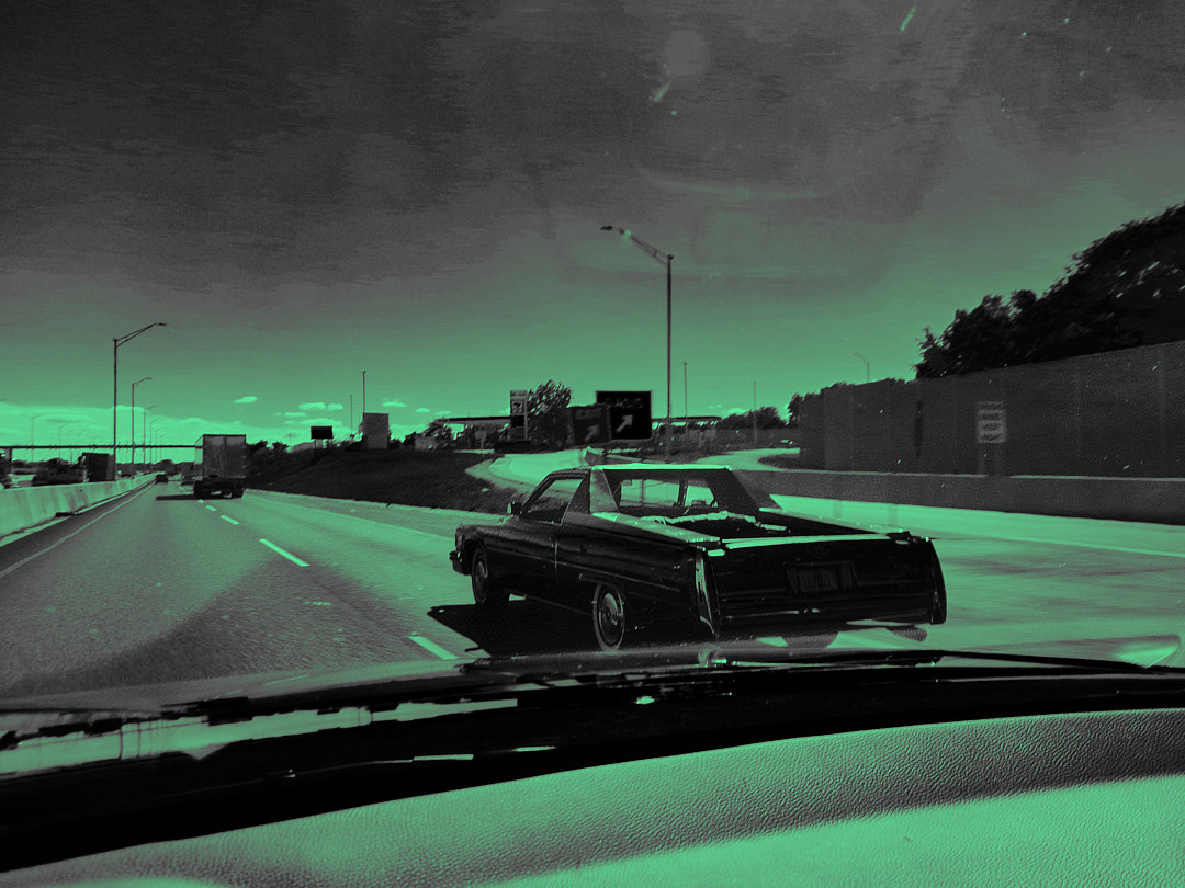 An old Cadillac pickup ahead on the interstate, seen through the windshield