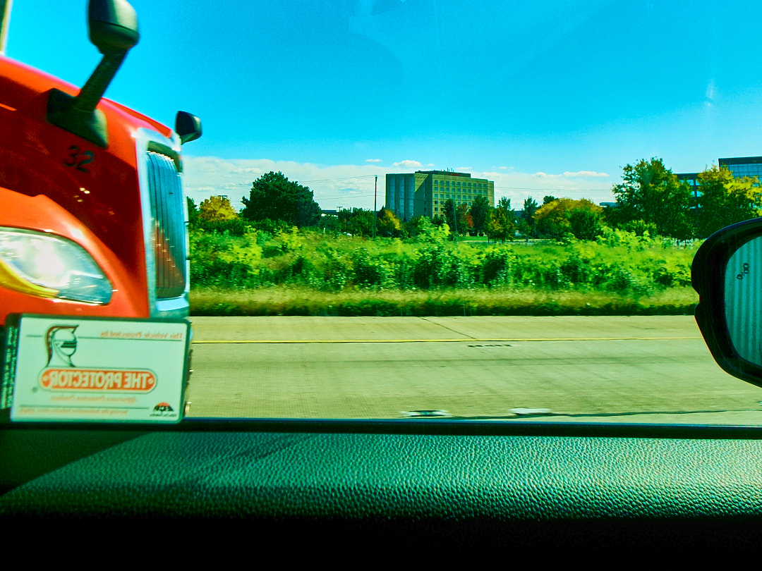 A truck cab alongside on the highway, office buildings beyond